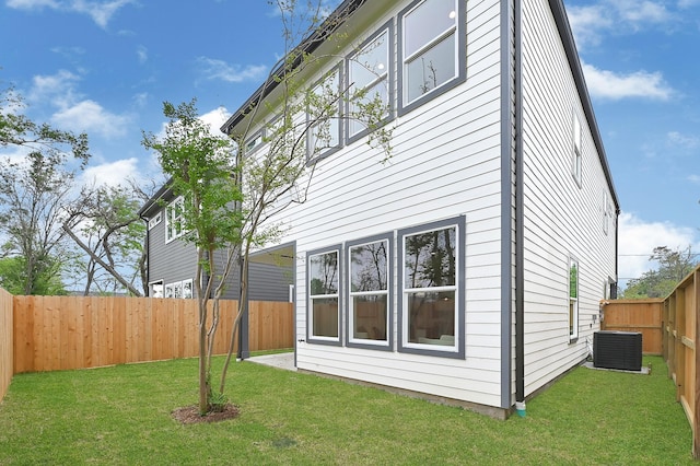 back of property with a fenced backyard, a lawn, and central AC