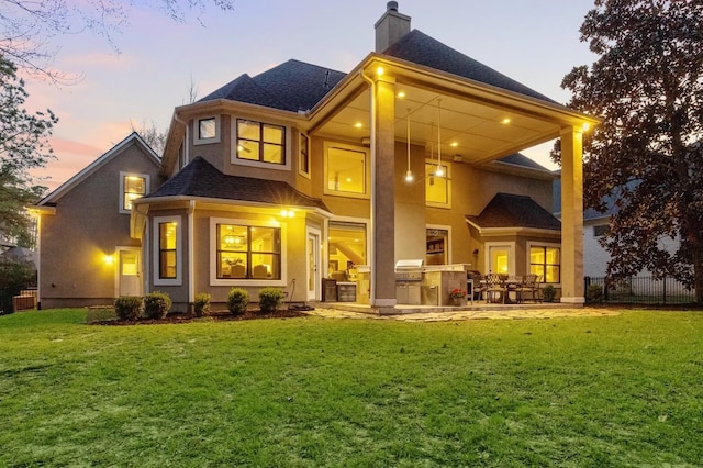 271 W Pines Dr, Montgomery, TX 77356 - back of property at dusk featuring an outdoor kitchen, a chimney, stucco siding, roof with shingles, and a patio
