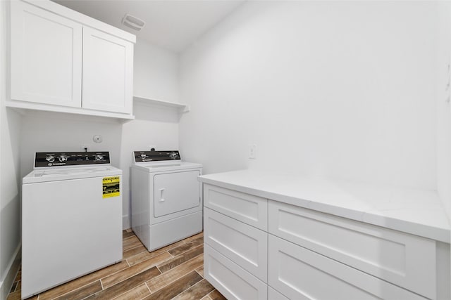 washroom featuring cabinet space, visible vents, wood finish floors, and washer and clothes dryer