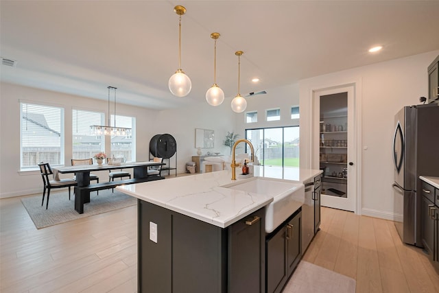 9603 Crescent Mill Dr, Missouri City, TX 77459 - kitchen featuring freestanding refrigerator, light stone countertops, light wood-type flooring, a sink, and a center island with sink