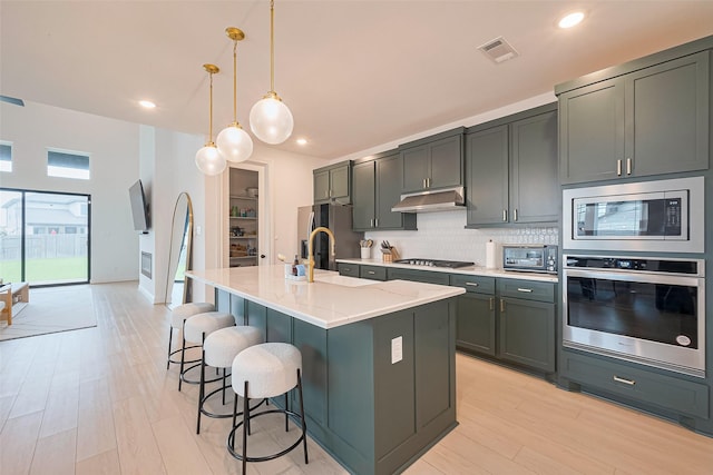 9603 Crescent Mill Dr, Missouri City, TX 77459 - kitchen featuring tasteful backsplash, visible vents, appliances with stainless steel finishes, a kitchen island with sink, and under cabinet range hood