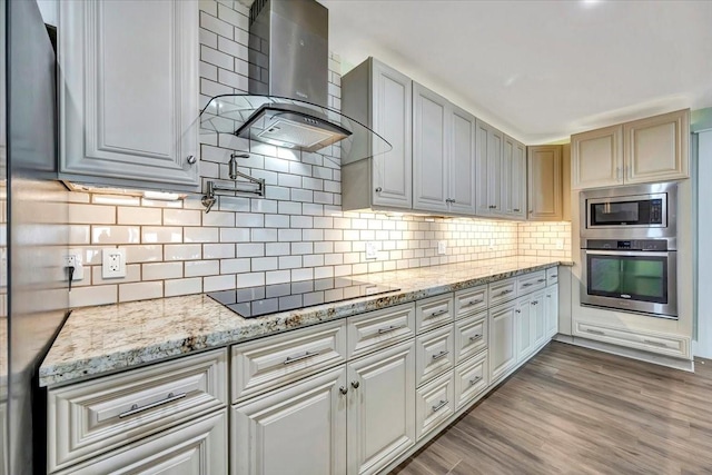 126 Tamana Dr, Tiki Island, TX 77554 - kitchen with light stone counters, backsplash, wall chimney exhaust hood, wood finished floors, and appliances with stainless steel finishes