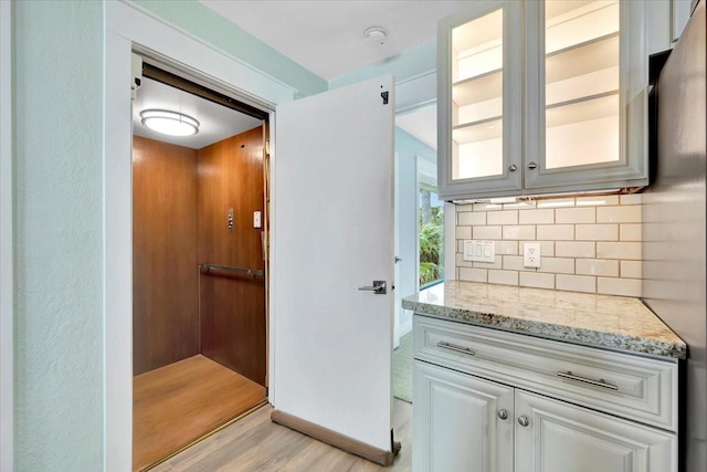126 Tamana Dr, Tiki Island, TX 77554 - kitchen featuring light stone countertops, light wood-style floors, glass insert cabinets, and decorative backsplash