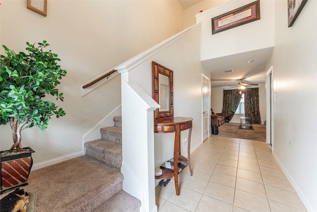 stairs with carpet, baseboards, ceiling fan, a high ceiling, and tile patterned flooring