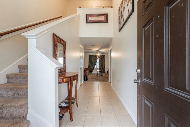 foyer with baseboards, ceiling fan, stairway, a high ceiling, and light tile patterned floors