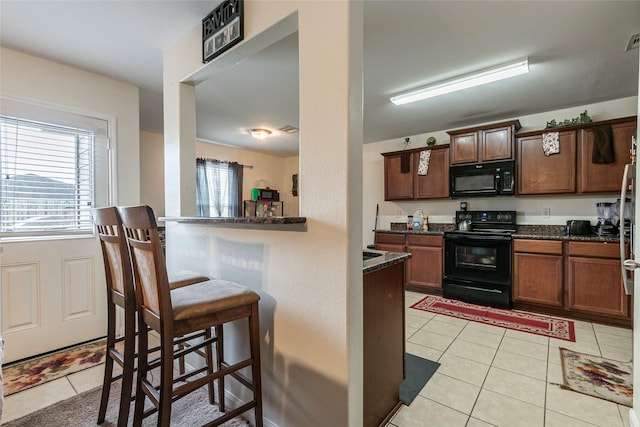 kitchen featuring black appliances, a breakfast bar, dark stone countertops, and light tile patterned floors