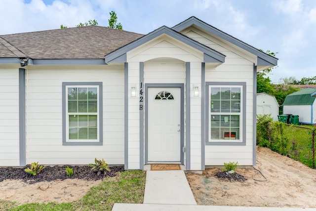 property entrance featuring fence and roof with shingles