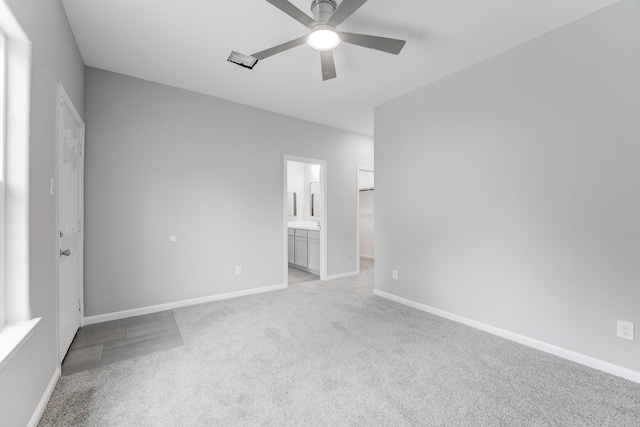 unfurnished bedroom with a ceiling fan, a spacious closet, ensuite bathroom, baseboards, and light colored carpet