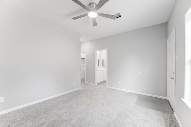 unfurnished bedroom featuring baseboards, ensuite bathroom, a ceiling fan, and light colored carpet