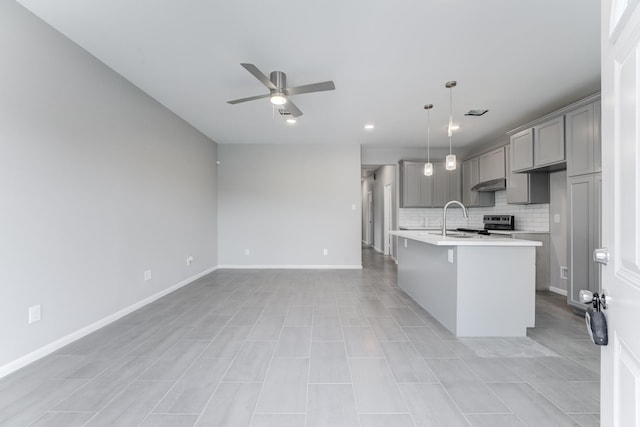 kitchen with gray cabinets, light countertops, decorative backsplash, a center island with sink, and ceiling fan
