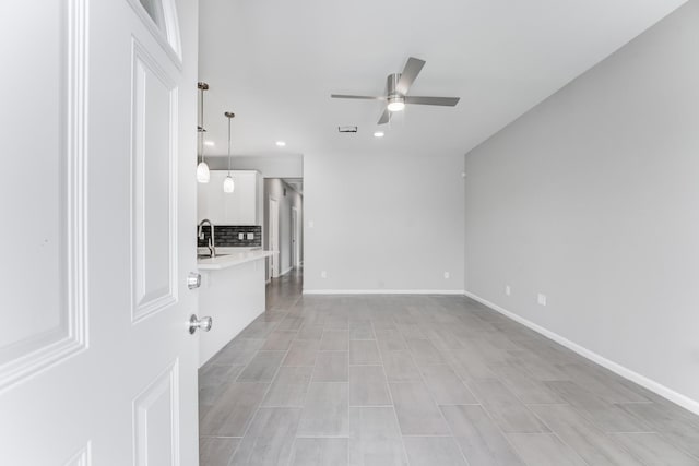 unfurnished living room with baseboards, recessed lighting, ceiling fan, and a sink