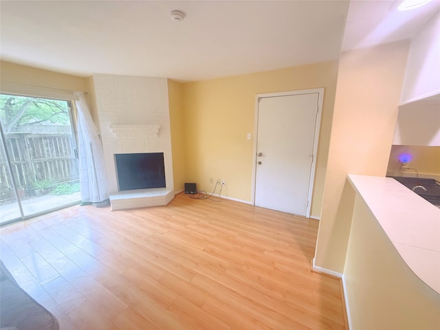 unfurnished living room with baseboards, light wood-style floors, and a brick fireplace
