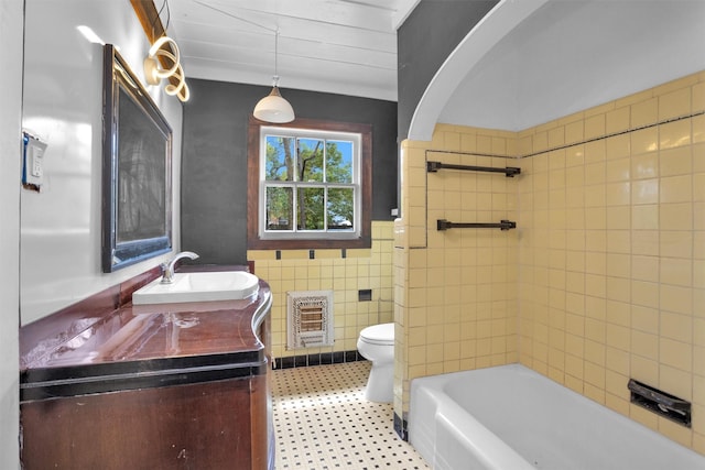 full bath featuring tile walls, a wainscoted wall, toilet, vanity, and heating unit