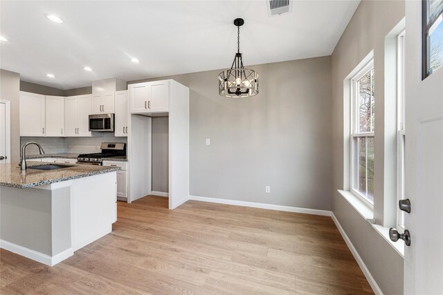 kitchen with white cabinets, stainless steel appliances, a sink, baseboards, and light stone countertops
