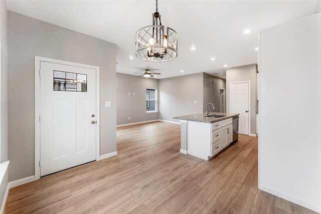 kitchen with light stone counters, a sink, light wood-style floors, dishwasher, and decorative light fixtures