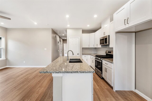 kitchen featuring light wood finished floors, a sink, a kitchen island with sink, appliances with stainless steel finishes, and white cabinetry
