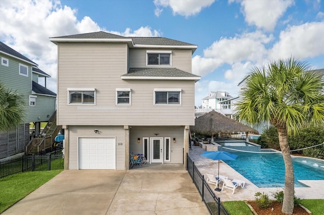 back of property with concrete driveway, roof with shingles, a fenced in pool, fence, and an attached garage