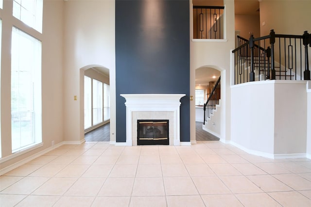 18719 Racquet Sports Way, Humble, TX 77346 - unfurnished living room with a towering ceiling, stairs, arched walkways, a tiled fireplace, and tile patterned flooring