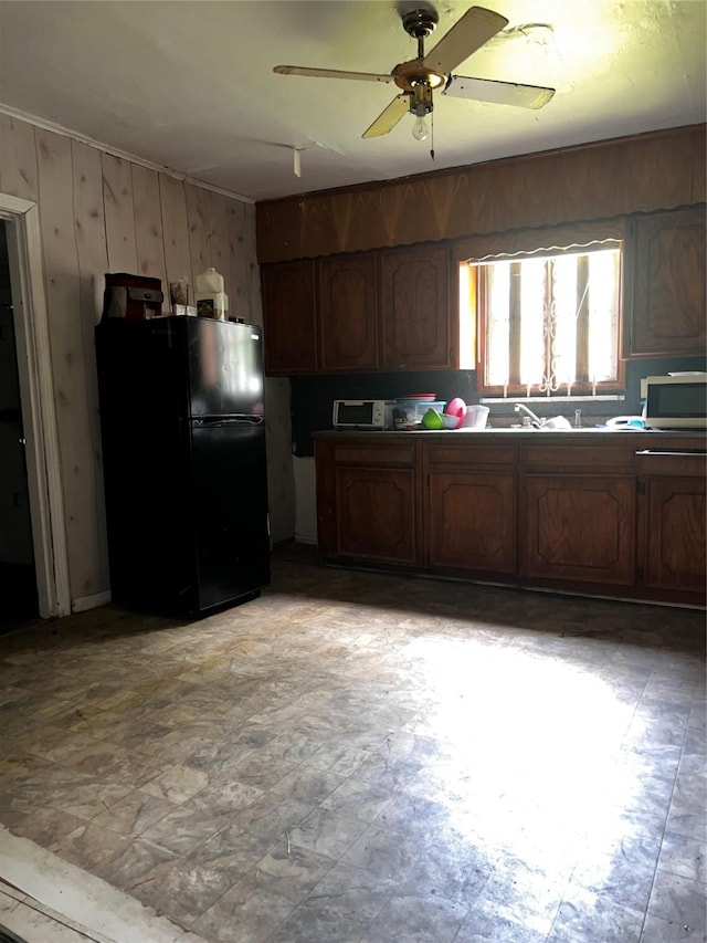 kitchen with freestanding refrigerator, a ceiling fan, stainless steel microwave, and wooden walls