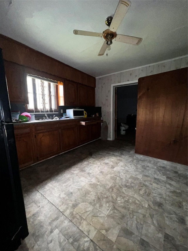 kitchen with wooden walls, ceiling fan, light floors, white microwave, and freestanding refrigerator