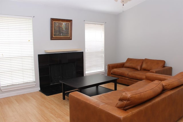 living area with light wood-style floors, a tiled fireplace, baseboards, and ceiling fan