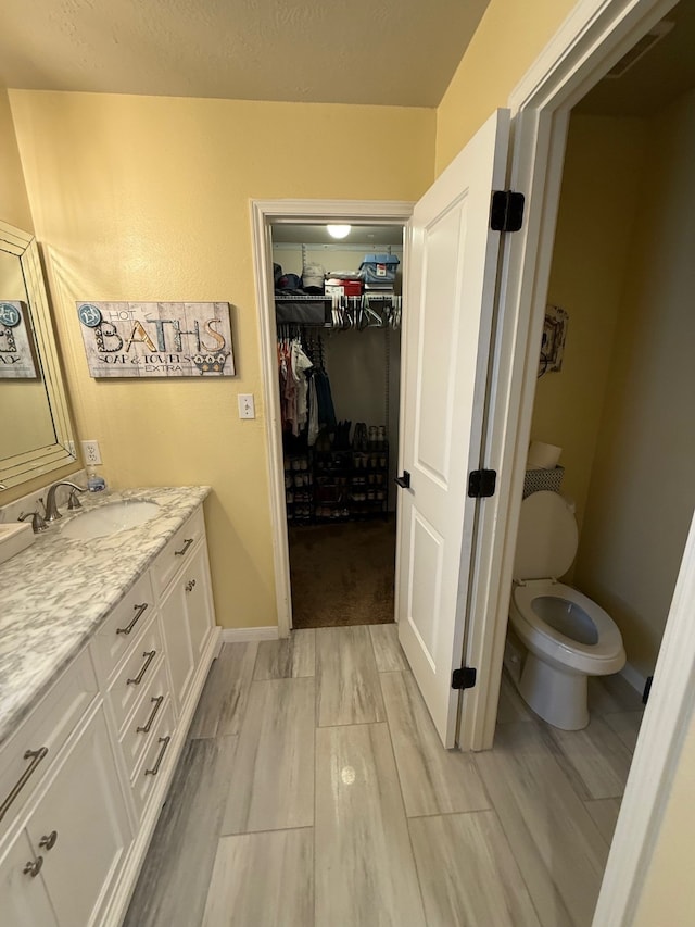 9319 Dalmore Ct, Houston, TX 77095 - bathroom featuring vanity, a spacious closet, wood finish floors, toilet, and baseboards
