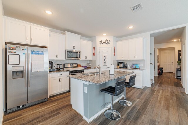 31511 Kailua Dr, Hockley, TX 77447 - kitchen featuring appliances with stainless steel finishes, a sink, a breakfast bar, dark wood finished floors, and white cabinetry