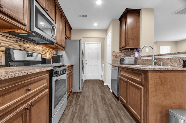 kitchen with stainless steel appliances, visible vents, a sink, dark wood-type flooring, and tasteful backsplash