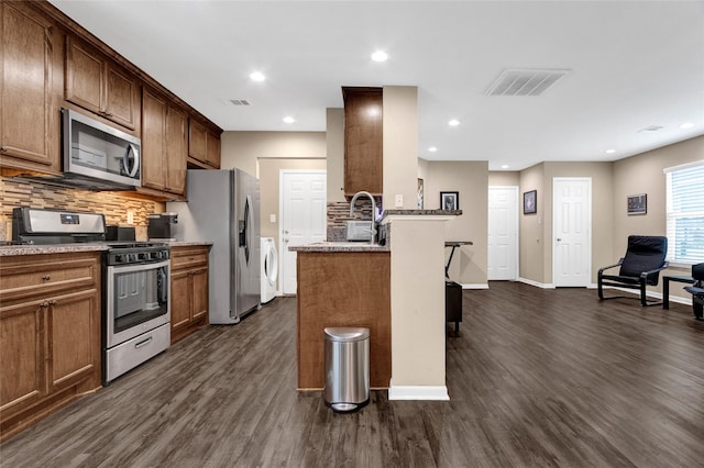 kitchen with dark wood finished floors, visible vents, washing machine and clothes dryer, and stainless steel appliances