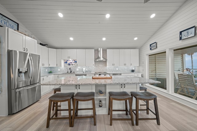 1407 John St, San Leon, TX 77539 - kitchen featuring stainless steel fridge with ice dispenser, wall chimney range hood, a sink, vaulted ceiling, and a breakfast bar