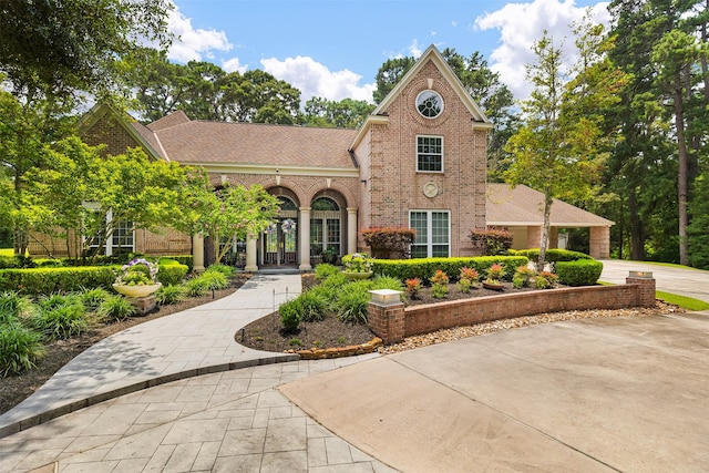 view of front facade featuring roof with shingles, brick siding, and curved driveway