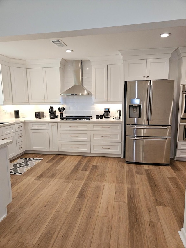kitchen with wall chimney range hood, light wood-style flooring, white cabinets, and stainless steel fridge
