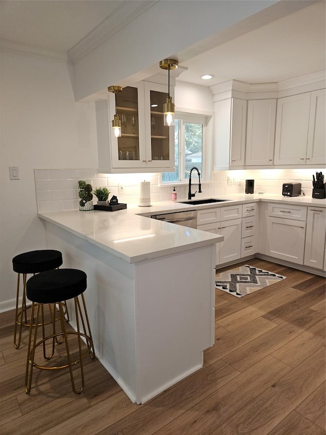 kitchen featuring a peninsula, white cabinets, crown molding, and a sink