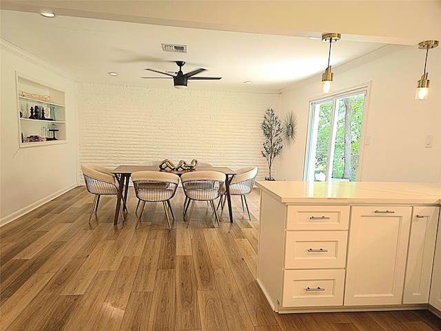 dining area featuring visible vents, a ceiling fan, light wood-style floors, crown molding, and brick wall