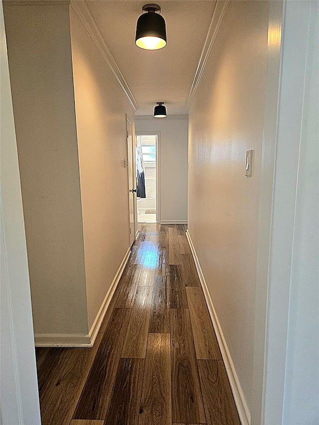 hallway featuring dark wood finished floors, crown molding, and baseboards