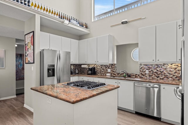 kitchen with stainless steel appliances, backsplash, a kitchen island, a sink, and light wood finished floors