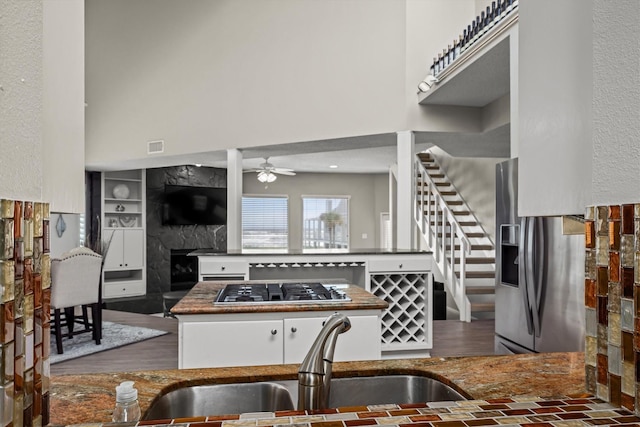 kitchen with stainless steel appliances, a high ceiling, a sink, a ceiling fan, and a fireplace