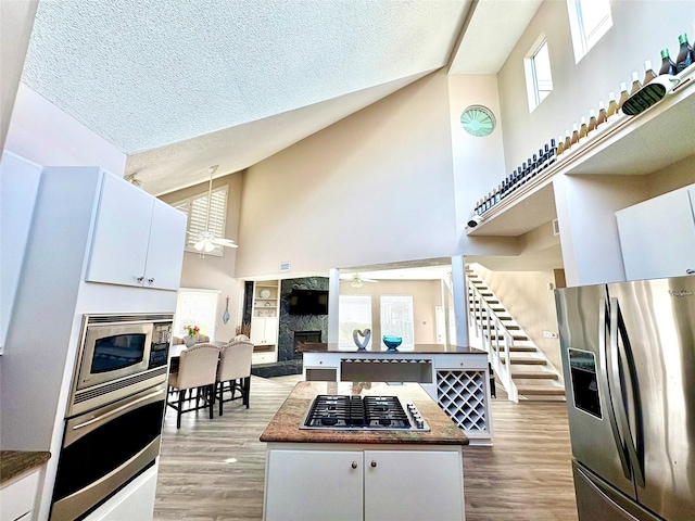 kitchen with high vaulted ceiling, a fireplace, dark countertops, a ceiling fan, and appliances with stainless steel finishes
