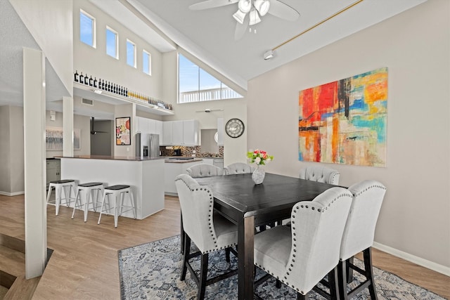 dining area with visible vents, light wood finished floors, baseboards, ceiling fan, and a towering ceiling