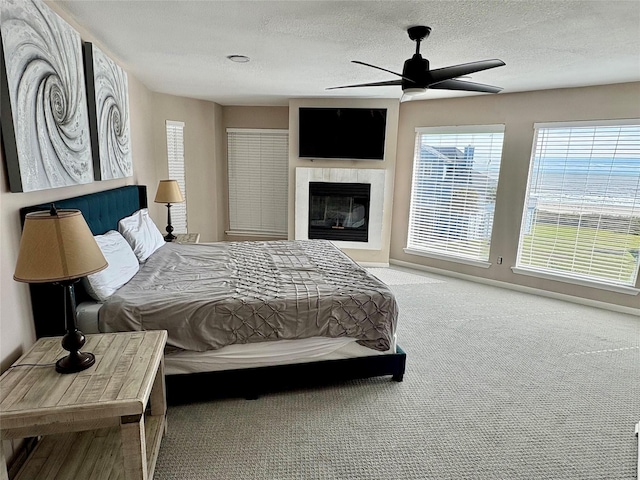 carpeted bedroom featuring a ceiling fan, a glass covered fireplace, and a textured ceiling