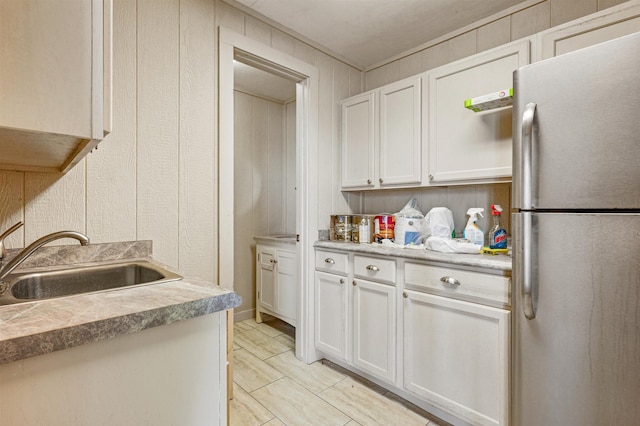 kitchen featuring freestanding refrigerator, light countertops, a sink, and white cabinetry
