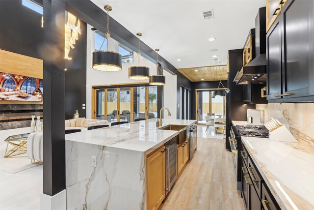 3902 Charleston St, Houston, TX 77021 - kitchen featuring black gas range, wall chimney exhaust hood, beverage cooler, a large island with sink, and light wood-type flooring