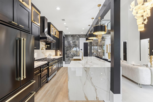 3902 Charleston St, Houston, TX 77021 - kitchen featuring premium appliances, wall chimney range hood, recessed lighting, light stone countertops, and glass insert cabinets
