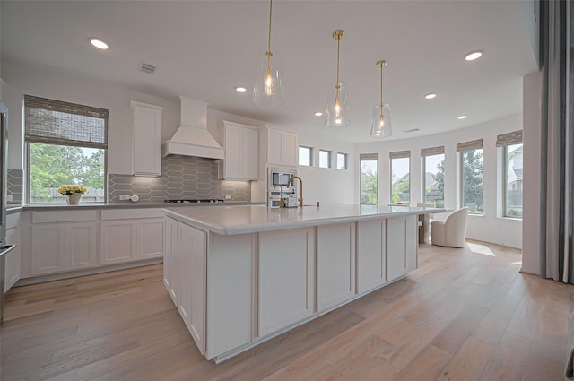 2611 Oakland Park Dr, Conroe, TX 77385 - kitchen with custom exhaust hood, stainless steel microwave, light wood-style flooring, healthy amount of natural light, and recessed lighting