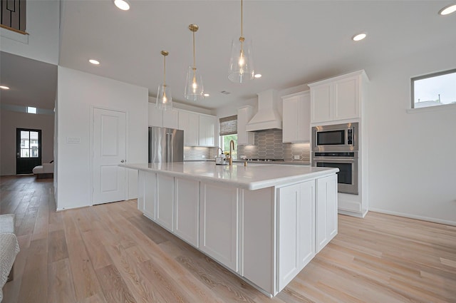 2611 Oakland Park Dr, Conroe, TX 77385 - kitchen with stainless steel appliances, light countertops, light wood-style flooring, white cabinets, and premium range hood