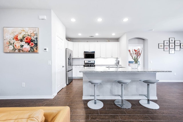 23818 Northwood Terrace Ln, Katy, TX 77493 - kitchen featuring white cabinetry, a breakfast bar area, dark wood-style flooring, arched walkways, and appliances with stainless steel finishes