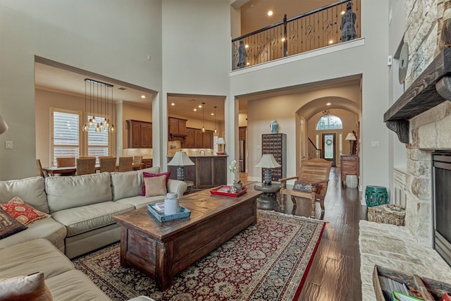 21610 Harbor Water Dr, Cypress, TX 77433 - living area featuring a stone fireplace, a chandelier, a towering ceiling, dark wood-type flooring, and arched walkways