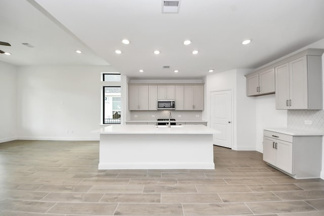14647 Cedar Elm Ct, Willis, TX 77318 - kitchen featuring stainless steel microwave, decorative backsplash, gray cabinetry, light countertops, and light wood-style flooring