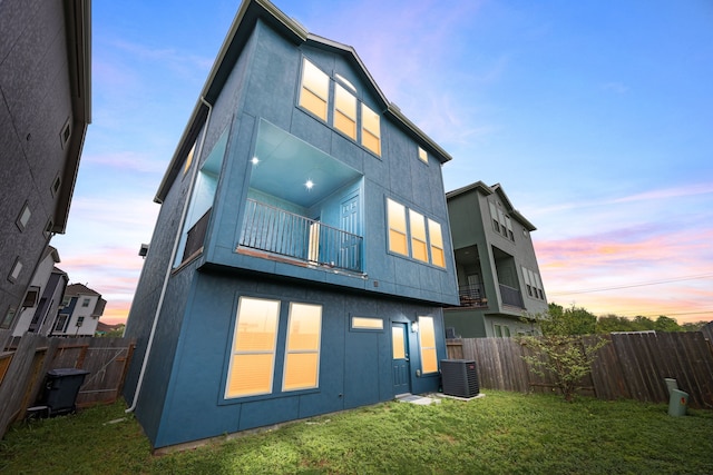 rear view of property with a lawn, fence, central AC, and a balcony
