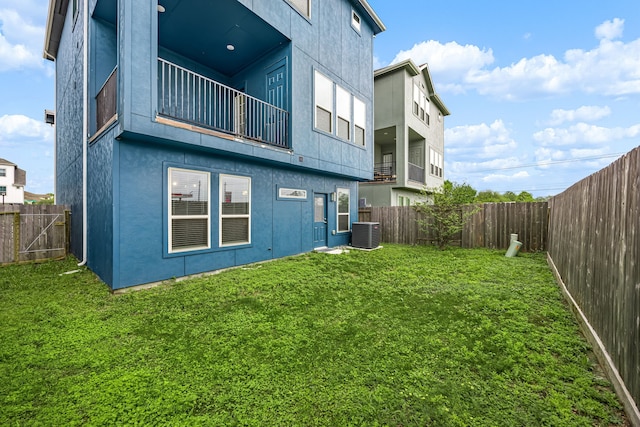 rear view of house with stucco siding, central AC unit, a fenced backyard, and a yard